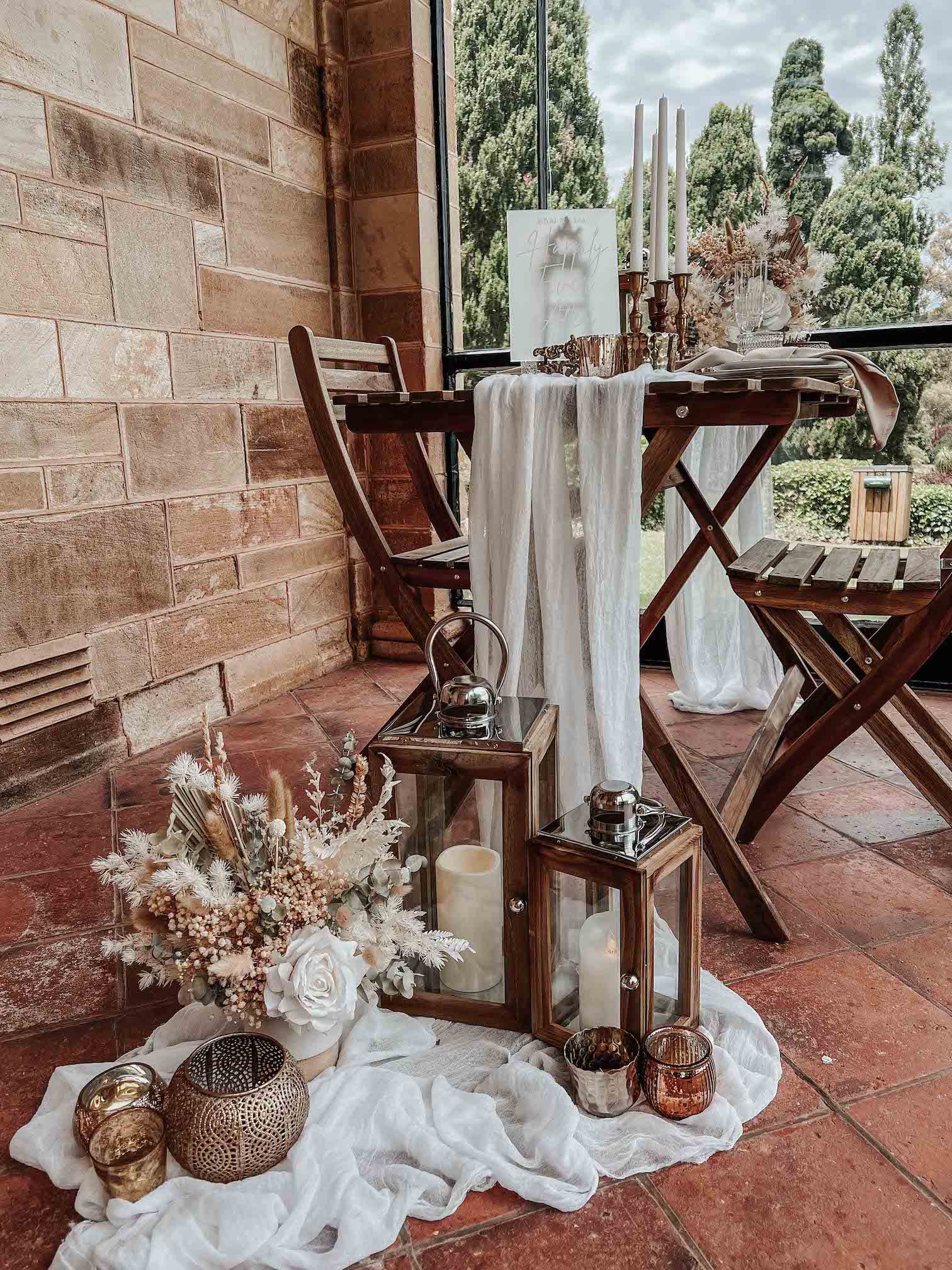 Close up details of romantic surprise proposal wooden table and chairs with lanterns and dried floral arrangements on the floor