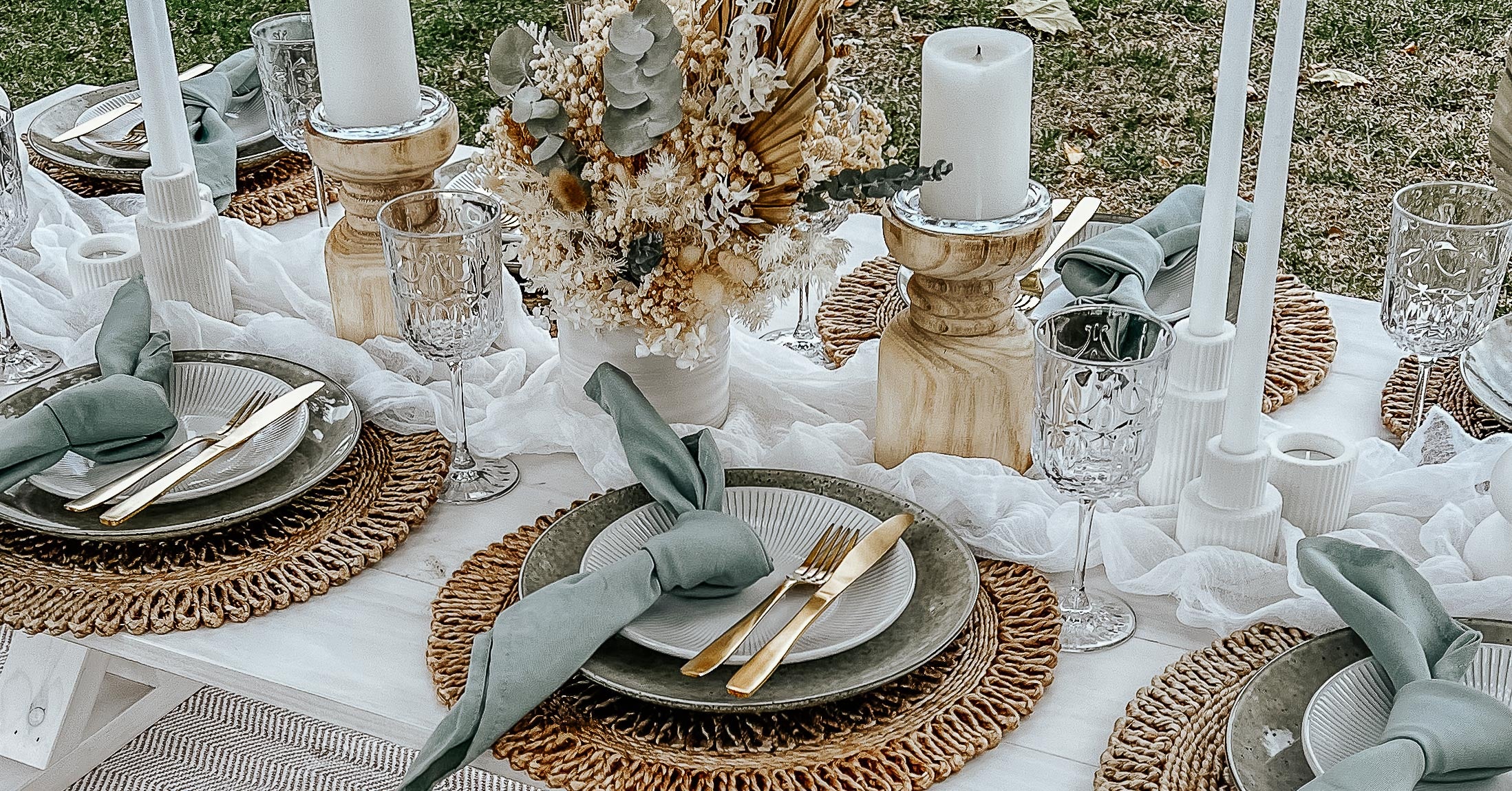 Sage green picnic set up in a park with dried flowers and natural candle holders