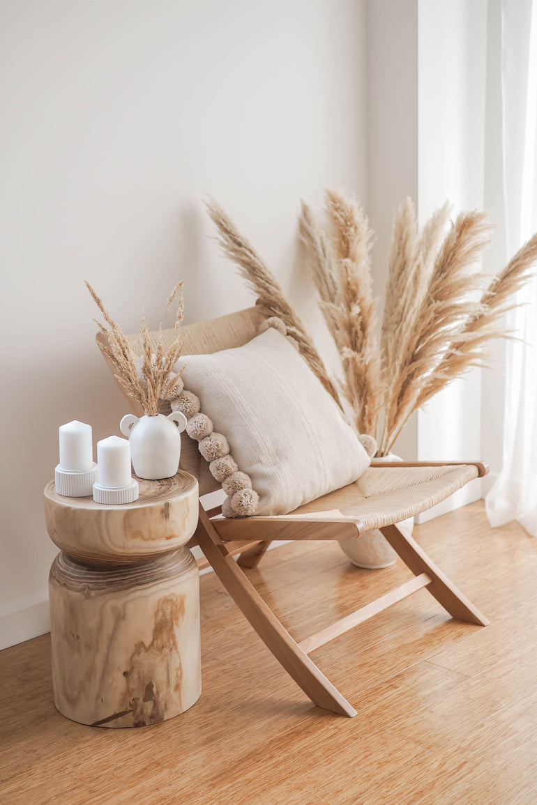 Large and small Mason candle holders displayed on a natural wood side table, boho jute rope chair, and large pot of pampas grass