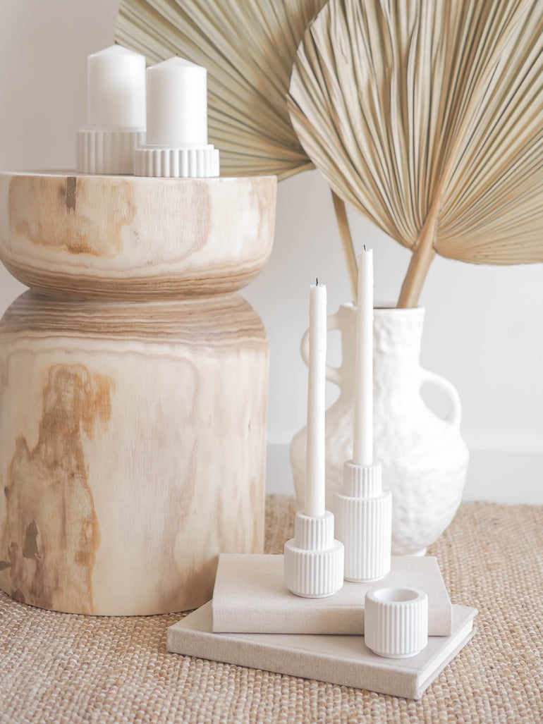 Palmer candle holders displayed on a stack of books in front of extra large palms in an irregular vase